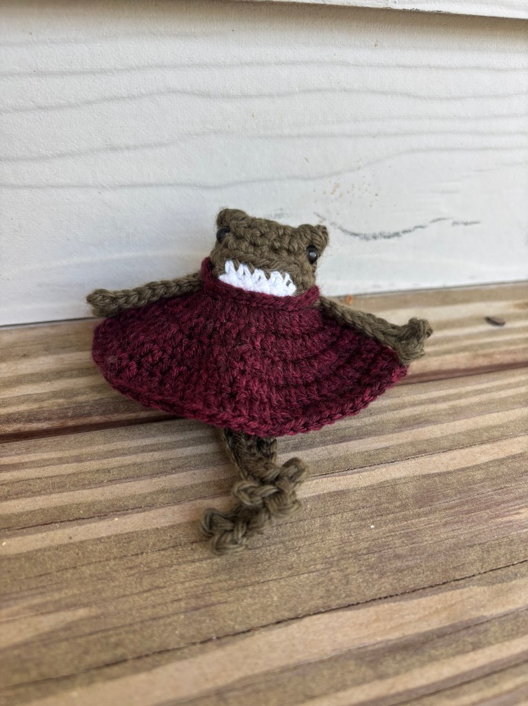 dark green crochet frog in babydoll dress plushie sitting with legs crossed